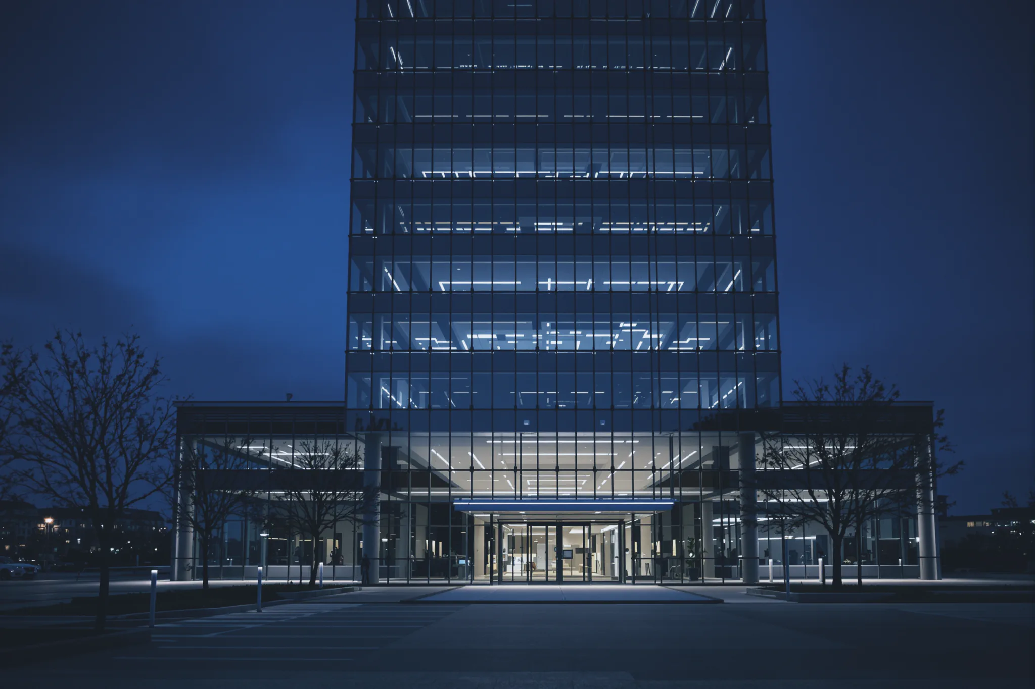 The entrance of a modern glass office tower at dusk.